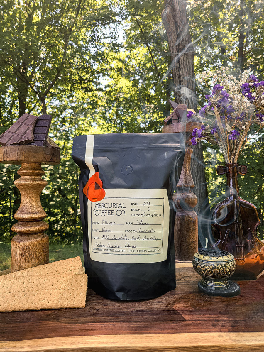 Bag of Mercurial Coffee Co's Ethiopian Sidamo Natural Process Decaf coffee, with notes of chocolate, graham cracker, and tobacco.